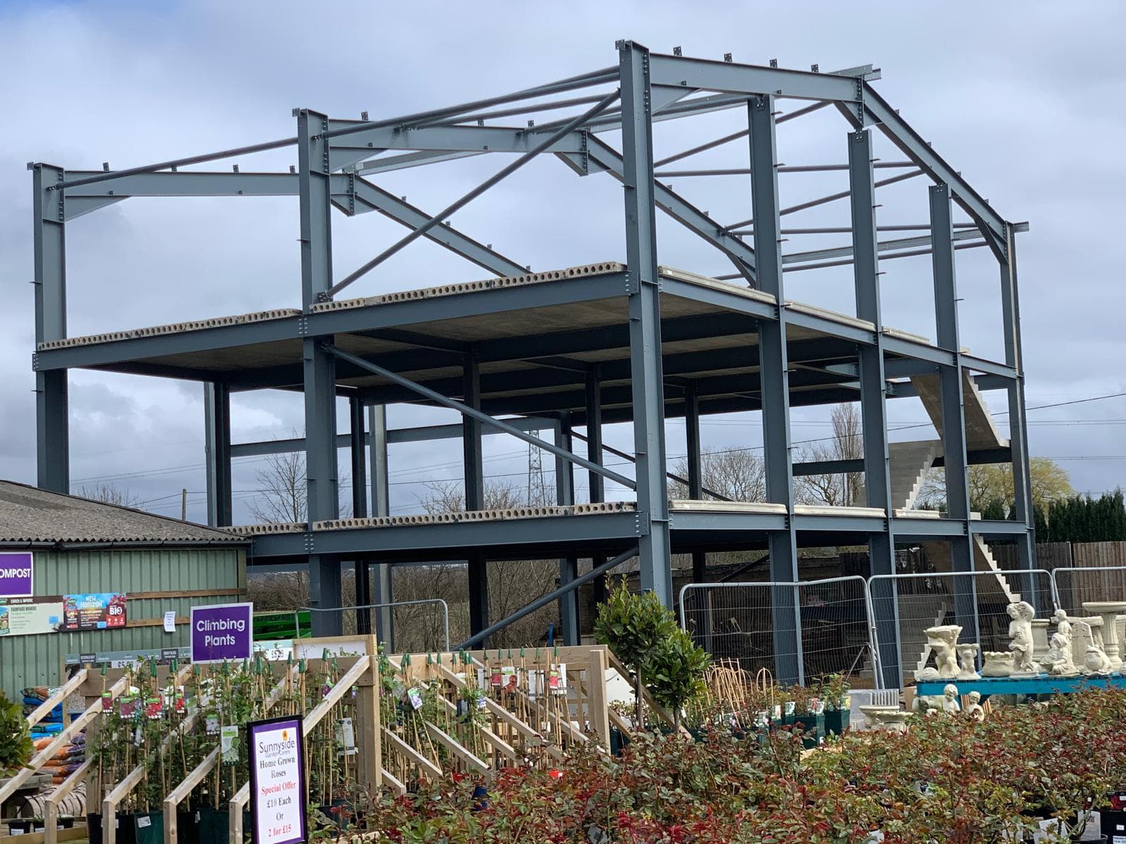 Multi-storey steel frame extension with concrete decks and stair core beside an active garden centre nursery