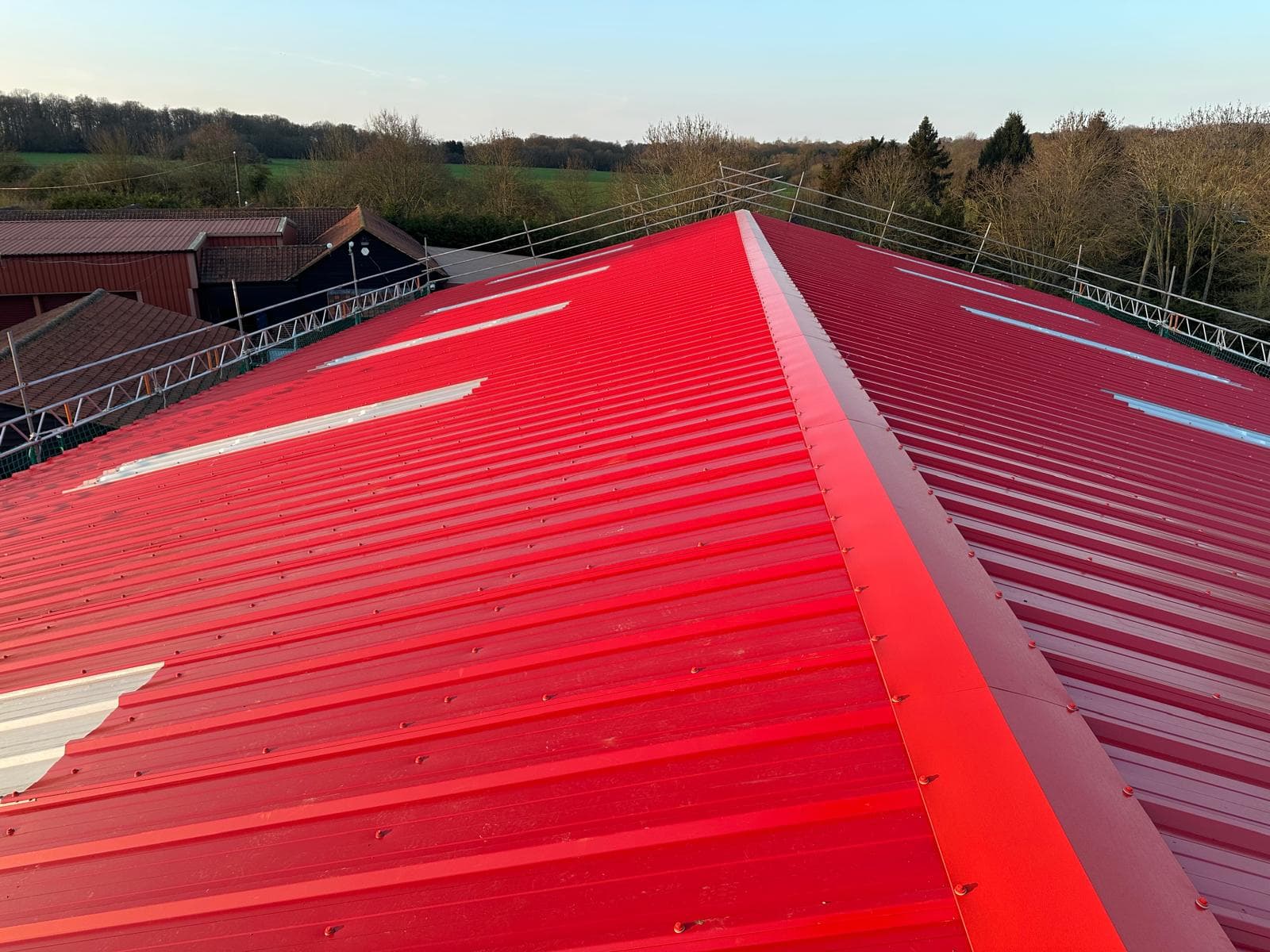 Red-finish roof overcladding across a wide industrial roof span